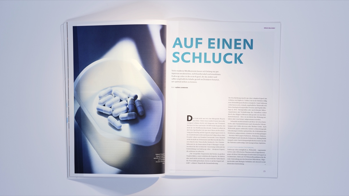 Photographed magazine spread for Evonik's "Elements" opened to the headline "Auf einen Schluck", with a close-up photo of blue-white capsules on a plate. Fotografierte Magazin-Doppelseite für Evoniks "Elements", aufgeschlagen bei der Überschrift "Auf einen Schluck", mit einer Nahaufnahme blau-weißer Kapseln auf einem Teller. Editorial photography / Editorialfotografie (Evonik Elements, KNSK): Robert Eikelpoth, Studio Eikelpoth, Düsseldorf.
