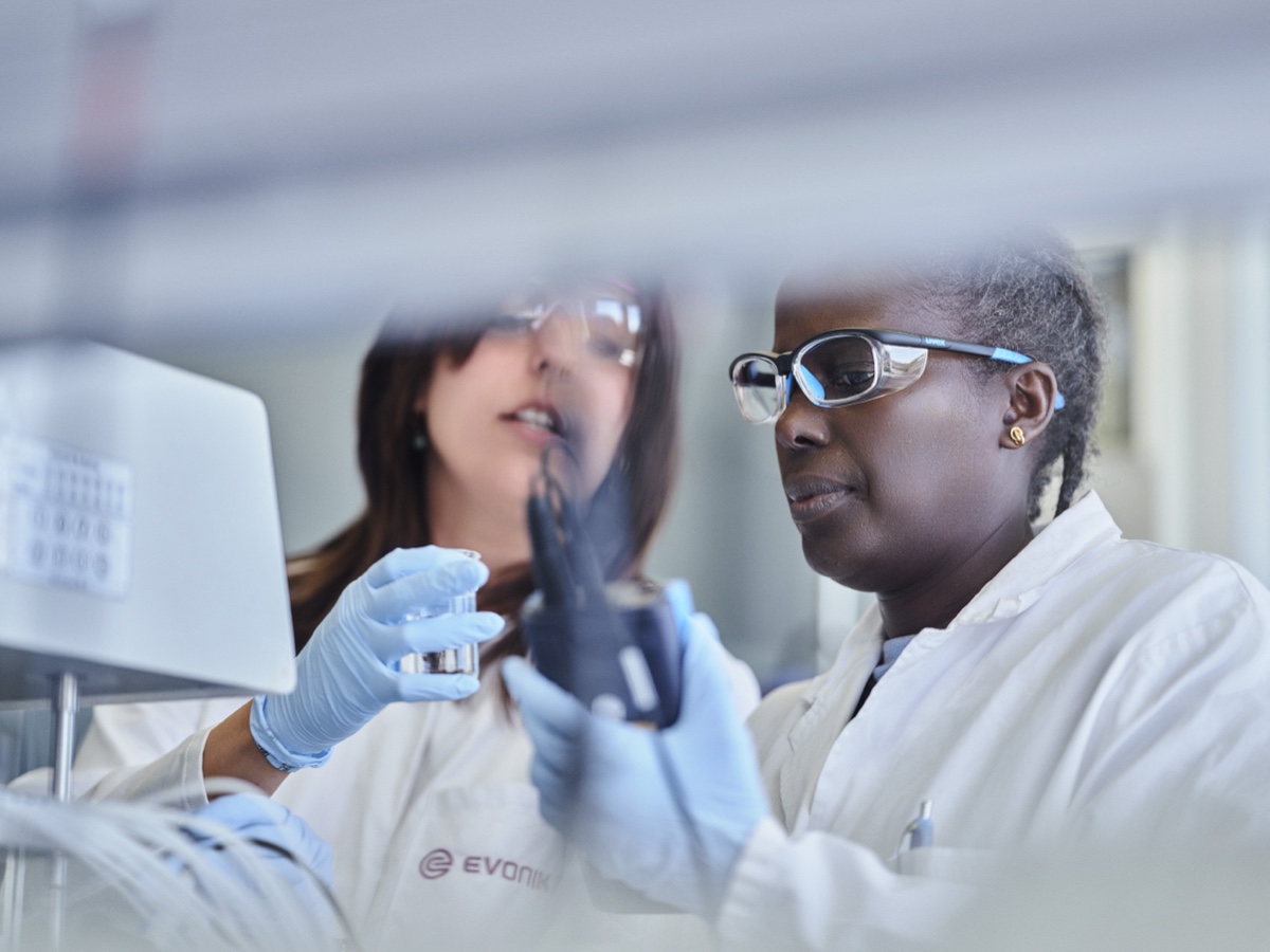 Two scientists in Evonik lab coats and safety glasses examining a capsule sample with a handheld measuring device in the laboratory. Zwei Wissenschaftlerinnen in Evonik-Laborkitteln und Schutzbrillen untersuchen im Labor mit einem Handmessgerät eine Kapselprobe. Editorial photography / Editorialfotografie (Evonik Elements, KNSK): Robert Eikelpoth, Studio Eikelpoth, Düsseldorf.
